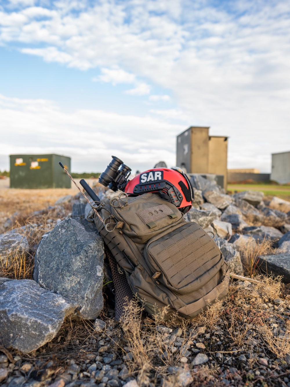 RADIO MANPACK leaning against the rocks with a SAR helmet and night-vision goggles on top, antennas up